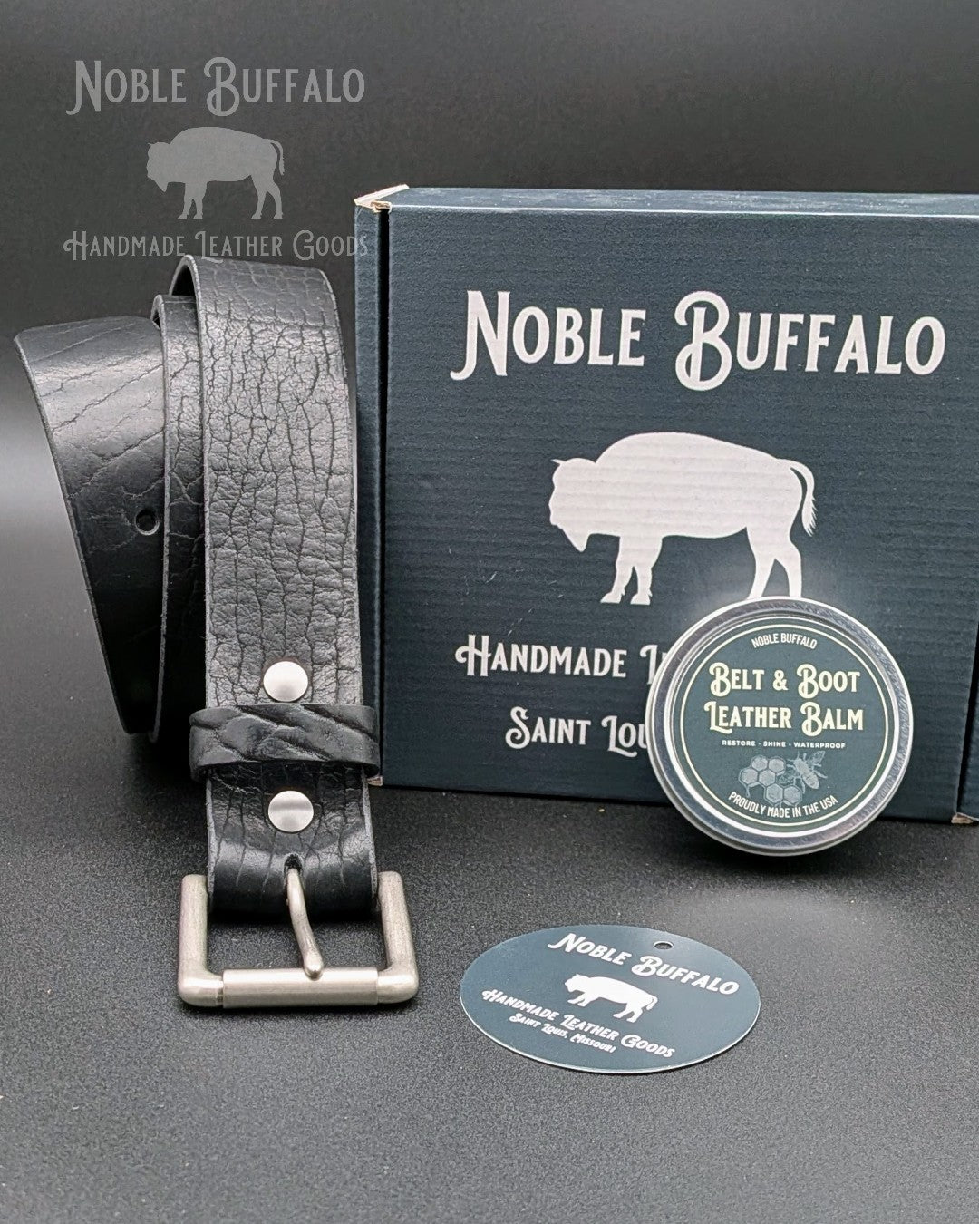 Handmade American full-grain leather belt in black bison leather with solid brass buckle, displayed with Noble Buffalo packaging and leather balm, made in St. Louis, USA.