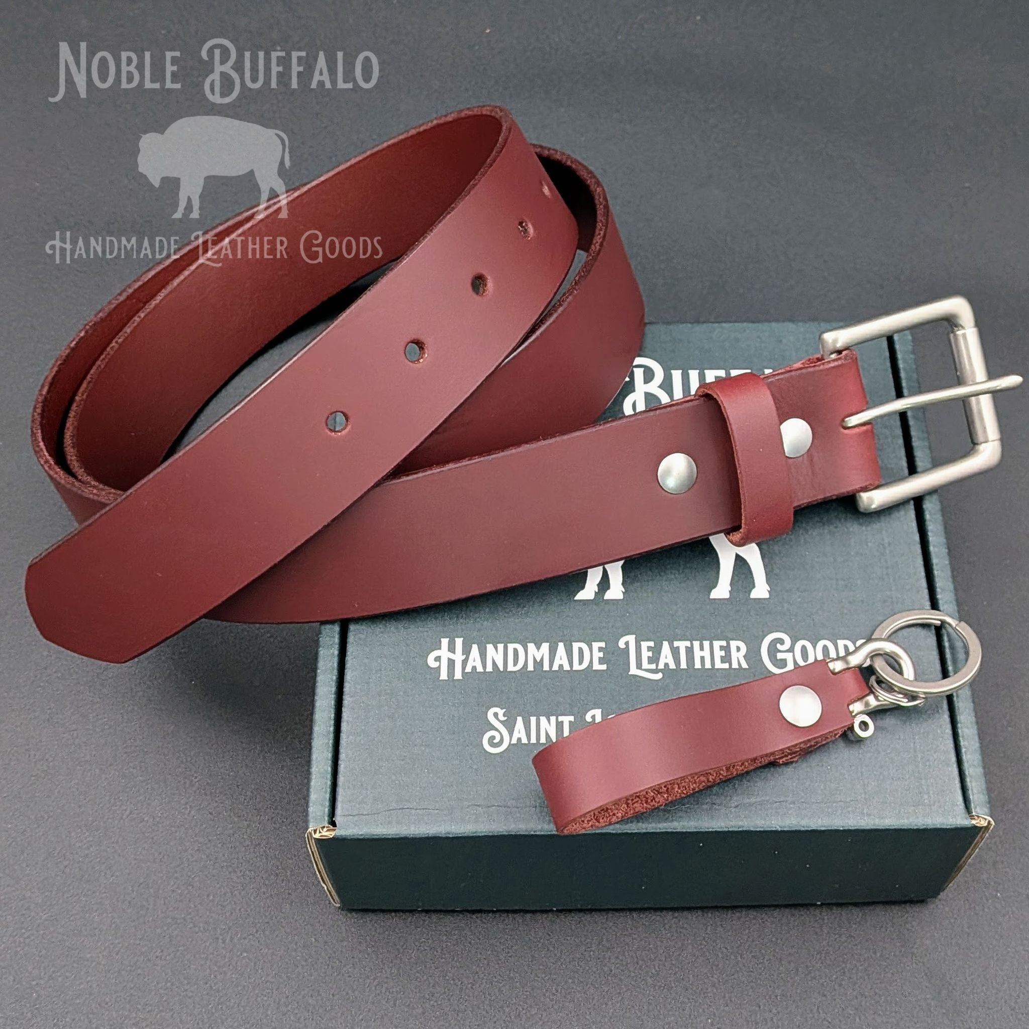 Burgundy latigo leather belt and matching keychain displayed on a Noble Buffalo gift box