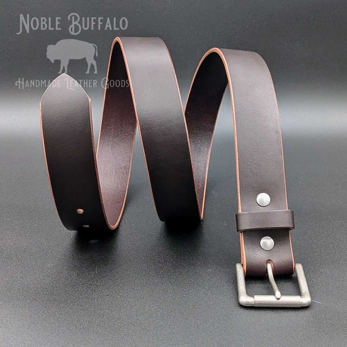 Dark brown Horween Illini Latigo leather belt arranged in waves, showing contrasting tan edges, a leather keeper, and silver-tone buckle.