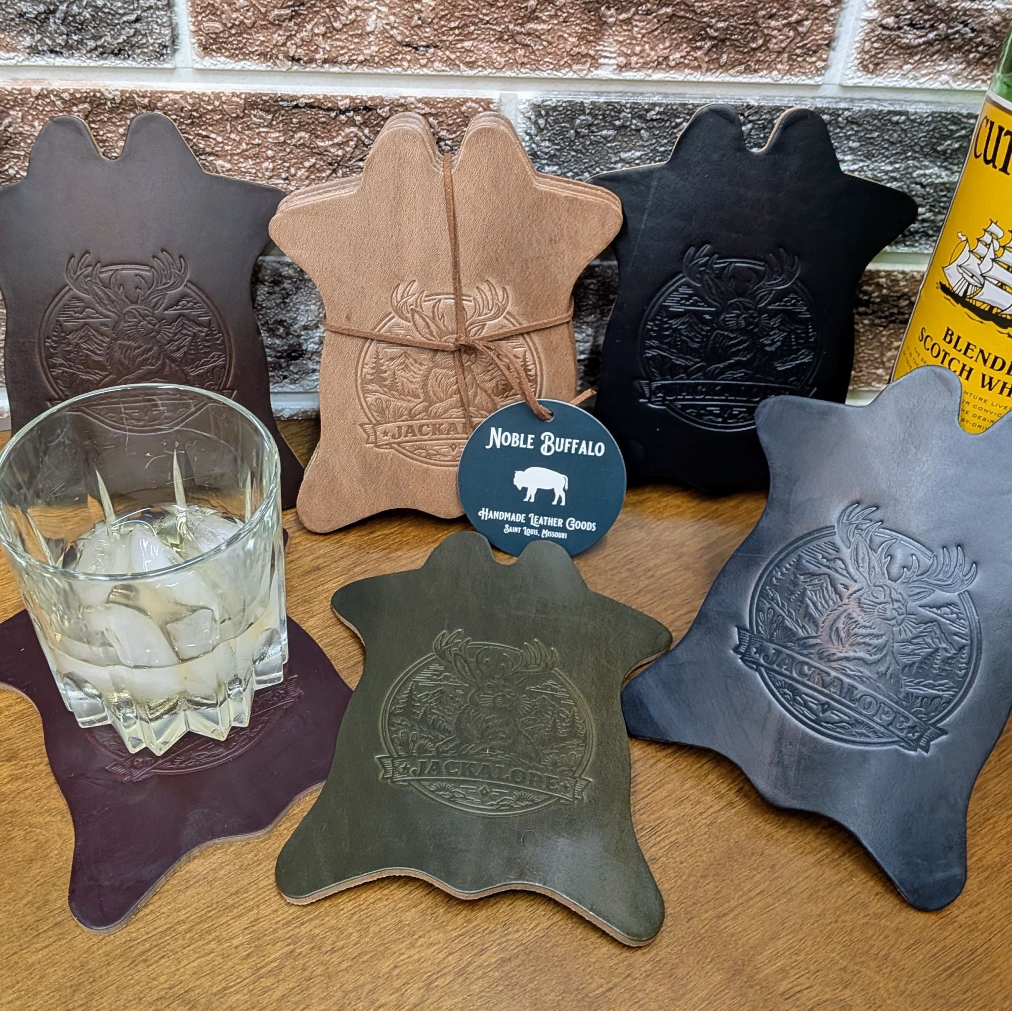 Handmade full grain leather drink coasters with embossed jackalope design, American made leather goods in multiple colors, built for everyday durability