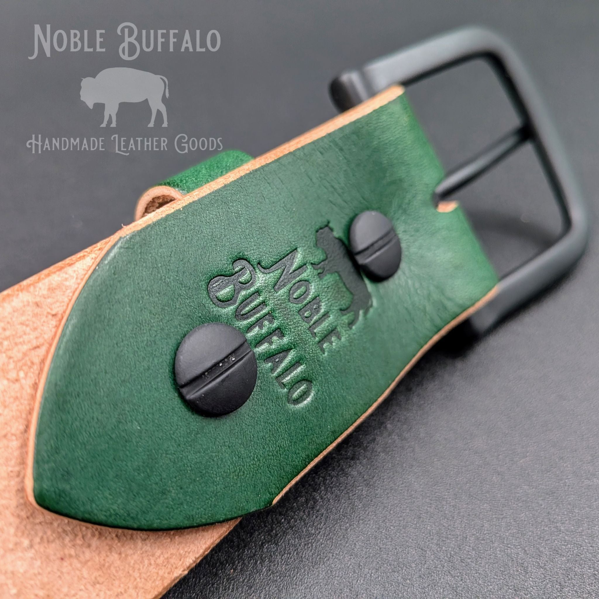 Close-up of the Noble Green latigo belt’s buckle attachment, showing the Noble Buffalo stamp, black Chicago screws, and contrasting tan edges.