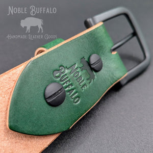 Close-up of the Noble Green latigo belt’s buckle attachment, showing the Noble Buffalo stamp, black Chicago screws, and contrasting tan edges.