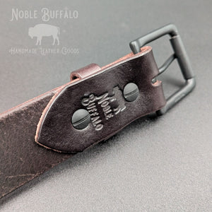 Close-up of the Roasted Arabica leather belt showing matte black Chicago screws, buckle, and Noble Buffalo maker’s mark.